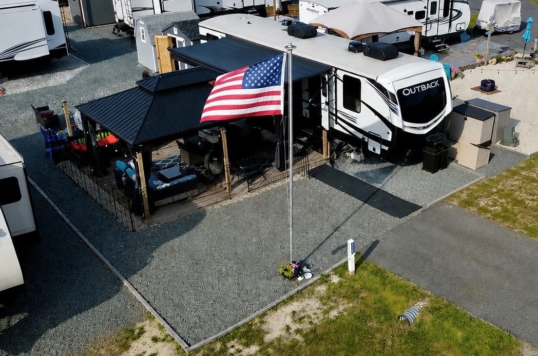Keystone Outback trailer beside a gated deck and gazebo, with an American flag in front